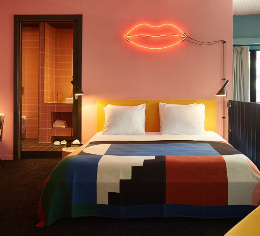 A double bed with colourful sheets with a neon lamp in a hotel room