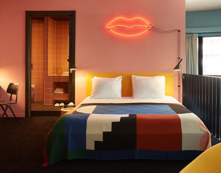 A double bed with colourful sheets with a neon lamp in a hotel room