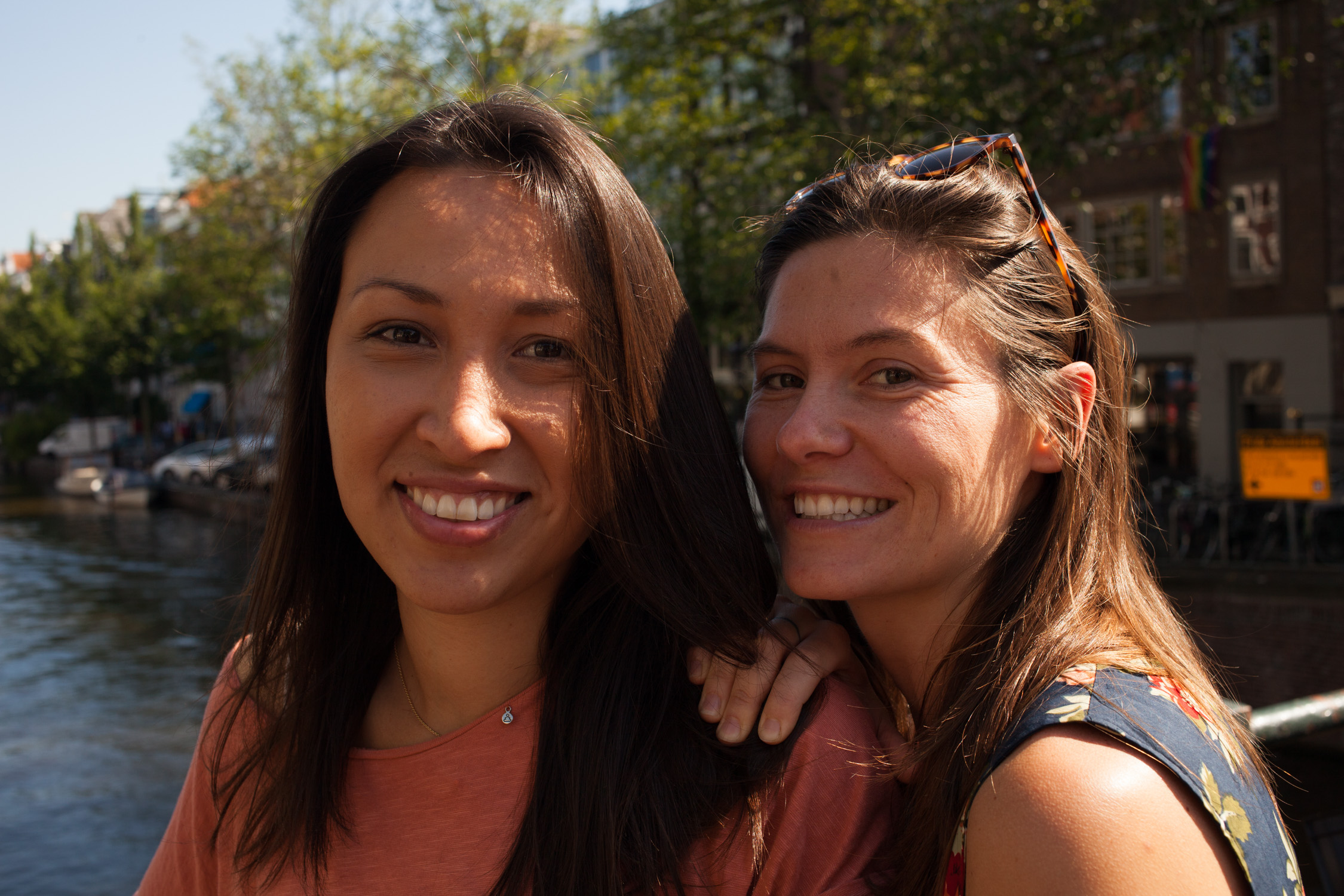 Two women standing next to each other and smiling in front of a canal