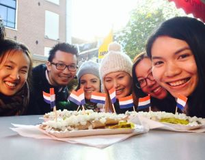 Five women and a man smiling over two Dutch herring with Dutch flags on them in Amsterdam